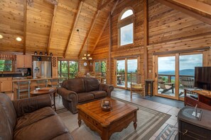 A spacious wooden cabin with a kitchen, living area with leather furniture, and a balcony with a view.