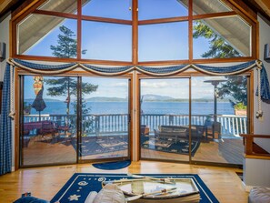 A large room with a glass door leading to a deck with a view of the sea. - San Juan Island, Washington Way Chalet #127 (Friday Harbor)