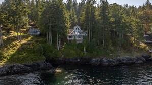 Une maison entourée d’une forêt dense, avec une côte rocheuse en premier plan.