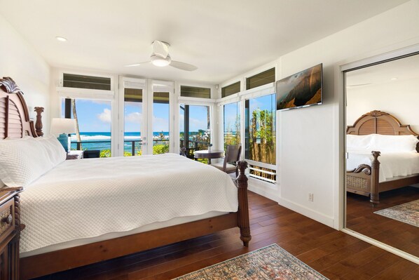 A spacious bedroom with a large bed, a ceiling fan, and a view of the ocean.