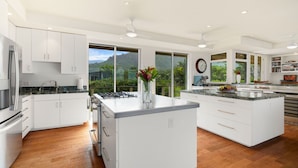 Una cocina moderna con armarios blancos, una isla central y vistas a vegetación exuberante.