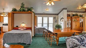 Ein Zimmer mit zwei Betten, einem Esstisch mit Barhocker, einem Deckenventilator und einer Vitrine.