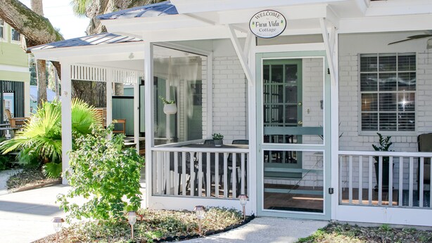 Ein weißes Cottage mit Veranda, einem Schild mit der Aufschrift 'Welcome to Punta Vida Cottage' und einem kleinen Garten mit Pflanzen und einem Weg.