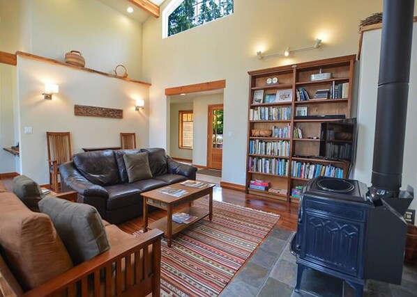 A cozy living room with a leather sofa, a coffee table, a bookshelf, and a wood-burning stove.