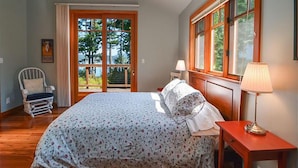 Une chambre avec un grand lit, une chaise, une table de chevet et une fenêtre donnant sur les arbres.