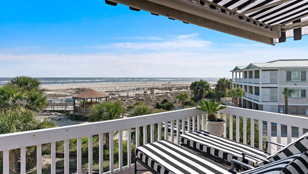 A balcony with white railings, two striped lounge chairs, and a view of the beach and ocean. - Relaxing Tybee Home Overlooking the Ocean (Tybee Island)