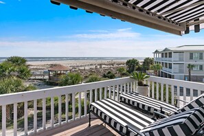 Un balcon avec des balustrades blanches, deux fauteuils de jardin à rayures et une vue sur la plage et l’océan.