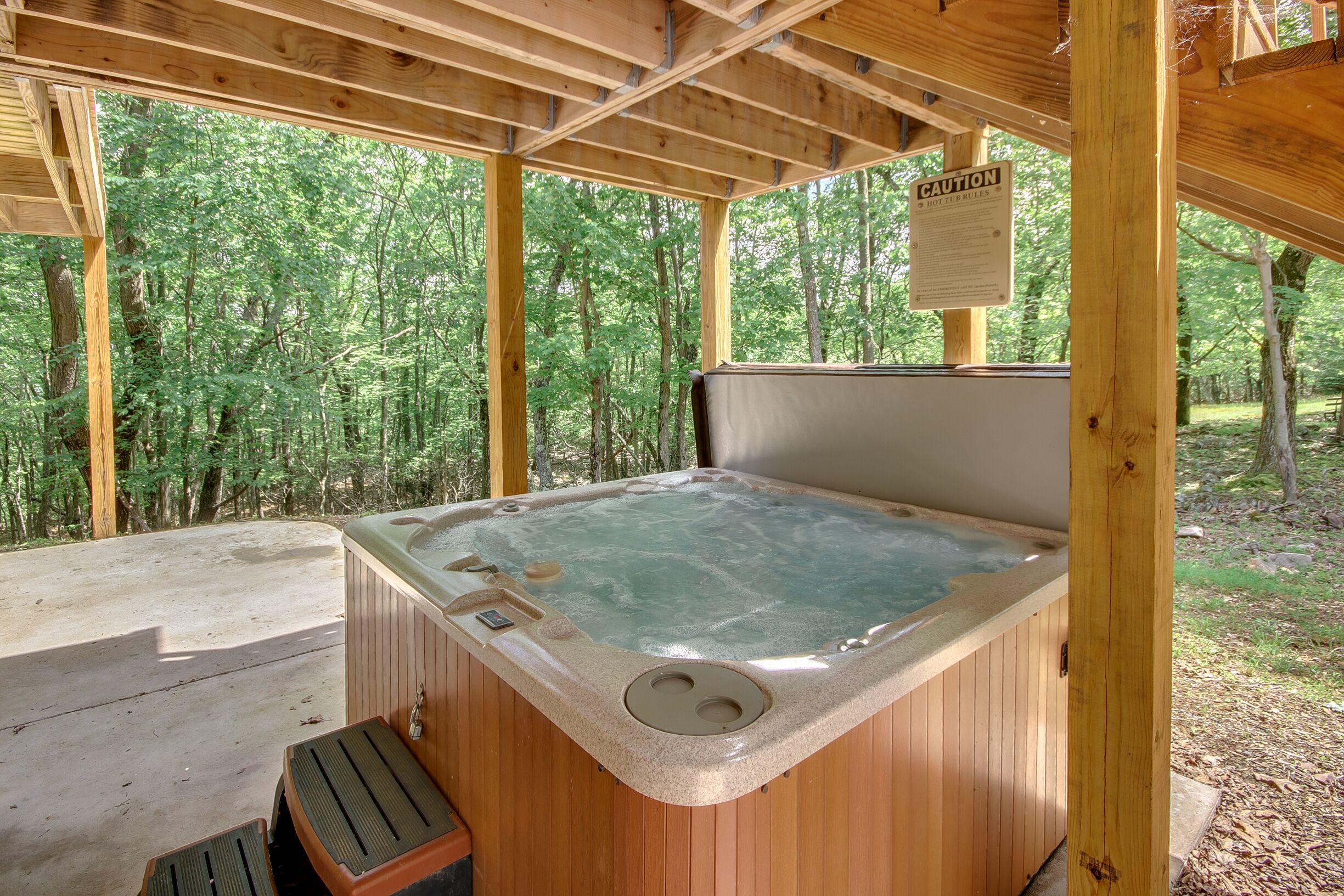 Un bain à remous dans un pavillon en bois, agrémenté d’un panneau d’avertissement, et entouré d’arbres.