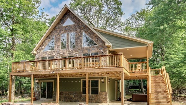 A two-story cabin with a stone facade, wooden deck, and a covered porch.