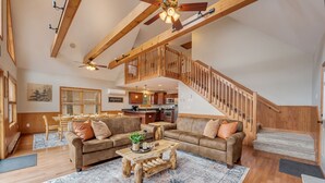 A spacious living room with a wooden staircase, a dining area, and a kitchen in the background.