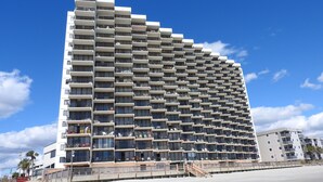 Een hoog hotel met meerdere balkons, uitzicht op het strand en een modern architectonisch ontwerp.