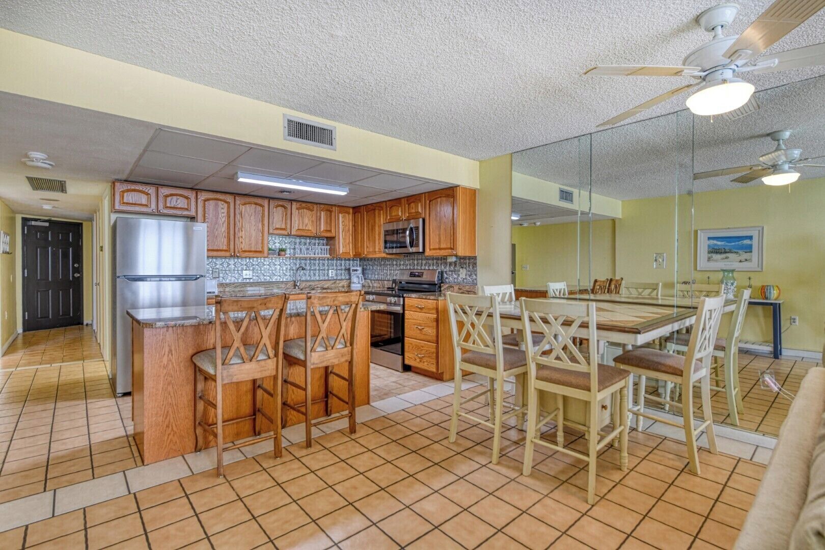 A kitchen with wooden cabinets, a stainless steel refrigerator, a microwave, and a dining area with a table and chairs.