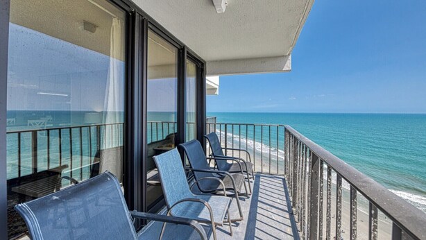 Een balkon met stoelen, een glazen deur en uitzicht op zee.