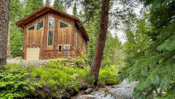 Eine Holzhütte mit Garage, umgeben von dichtem Wald und einem Bach.
