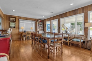 A dining area with a glass-top table, wooden chairs, a bookshelf, and a view of a staircase.