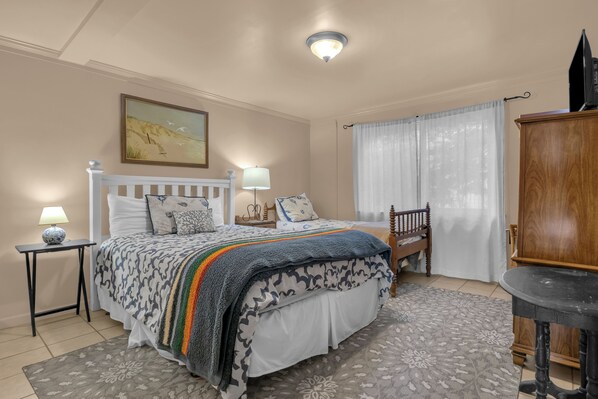 A bedroom with a bed, bedside tables, a lamp, a wooden cabinet, and a painting on the wall.