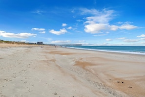 A beach with a pier extending into the water, sandy beach, and a building in the background.