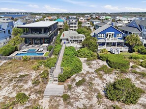 Zona residencial costeira com casas, piscina e um deck de madeira que dá para a praia.