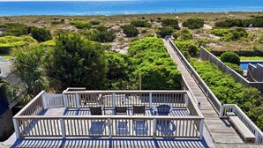 En træterrasse med udendørs møbler, med udsigt over en strand og et hav.