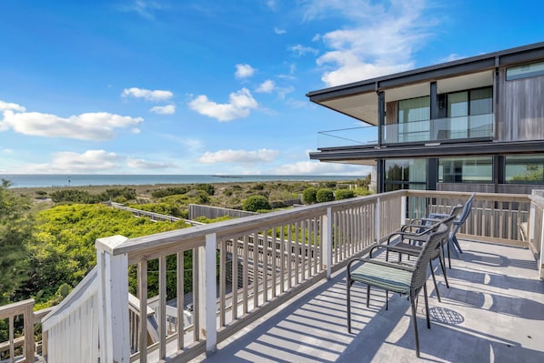 A balcony with a view of the ocean, a modern building, and outdoor furniture.