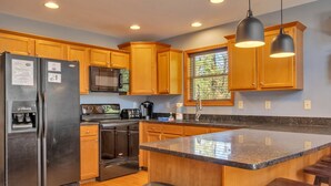 Una cocina moderna con armarios de madera, electrodomésticos de acero inoxidable, encimera de granito e iluminación colgante.