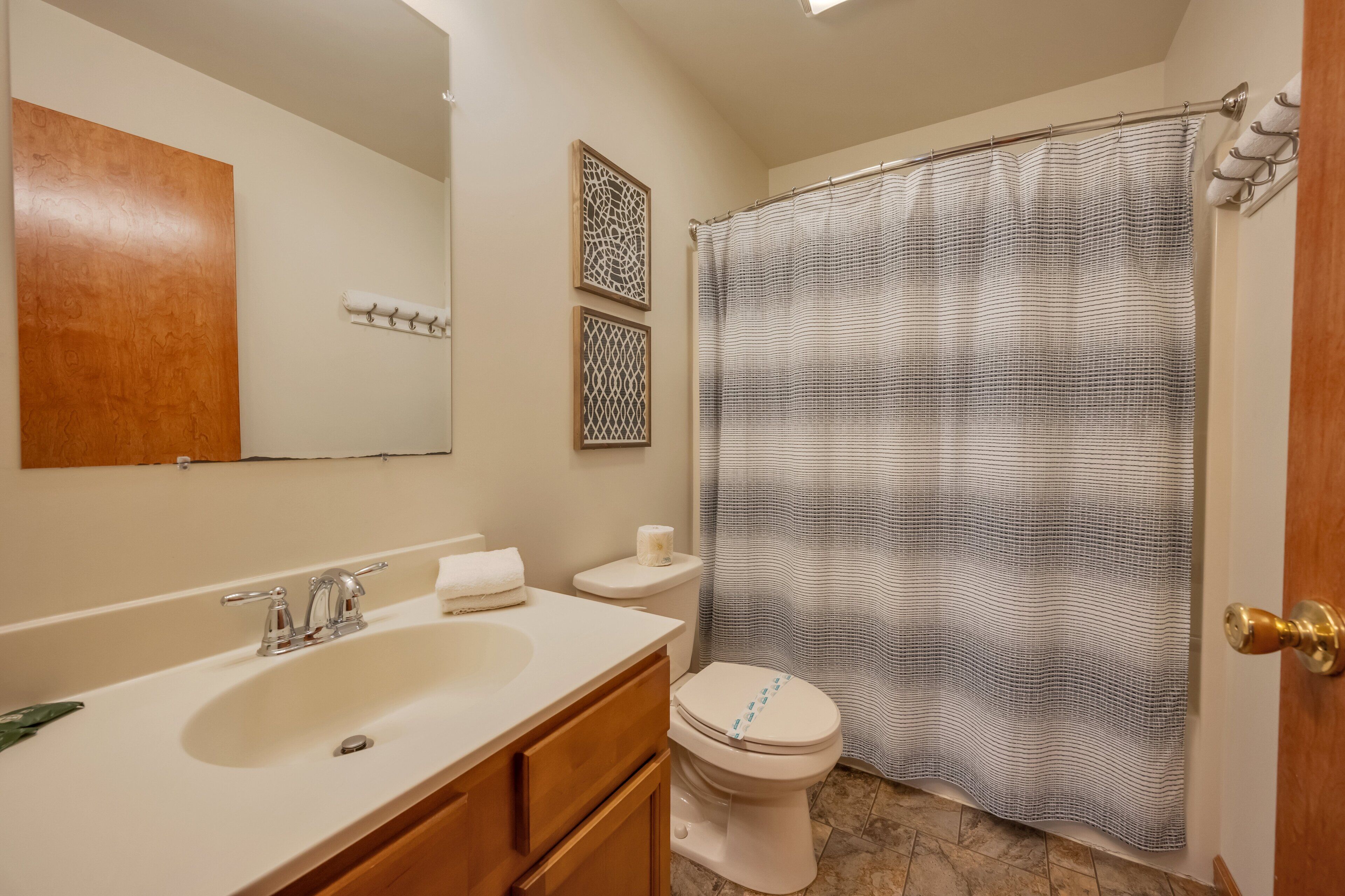 Une salle de bain avec un lavabo blanc, un meuble-lavabo en bois, des toilettes et un rideau de douche.