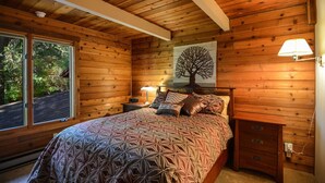 Un dormitorio de cabaña de madera con una cama, mesitas de noche y una lámpara.
