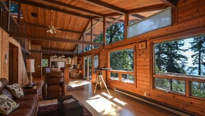 Un interior de cabaña espacioso con techos altos, paredes de madera, ventanas amplias, una zona de estar acogedora y un comedor.