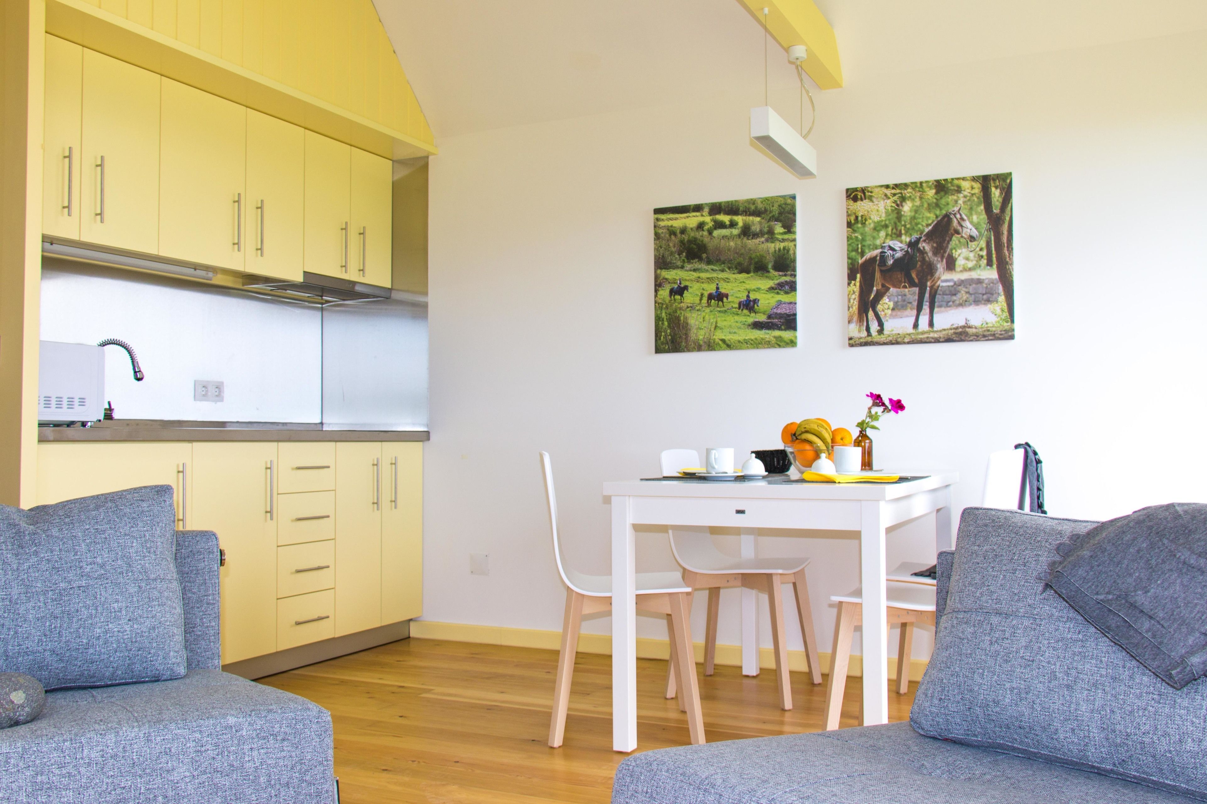 A compact living space with a kitchenette, a dining area with a white table and chairs, and two grey sofas.