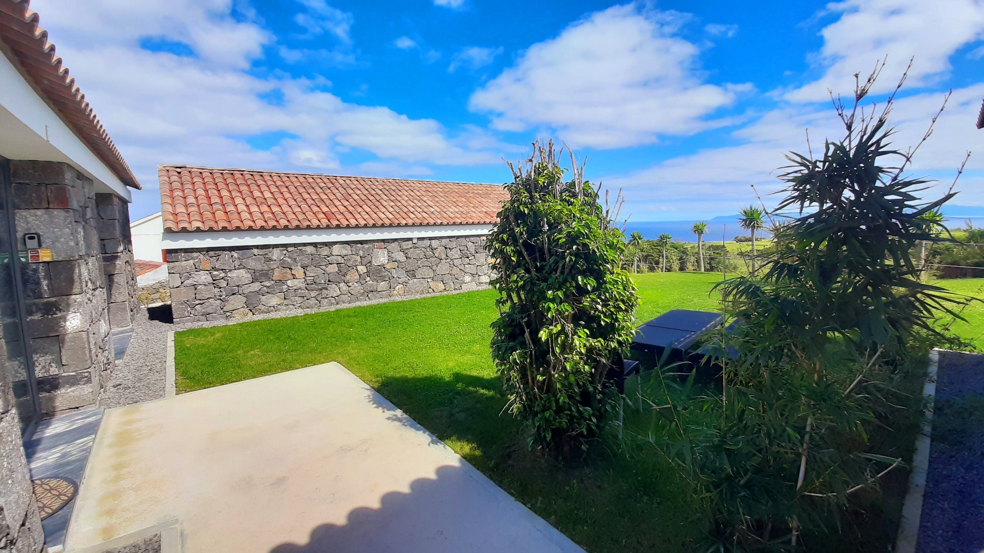 A stone house with a tiled roof, a grassy yard, and a view of the ocean.