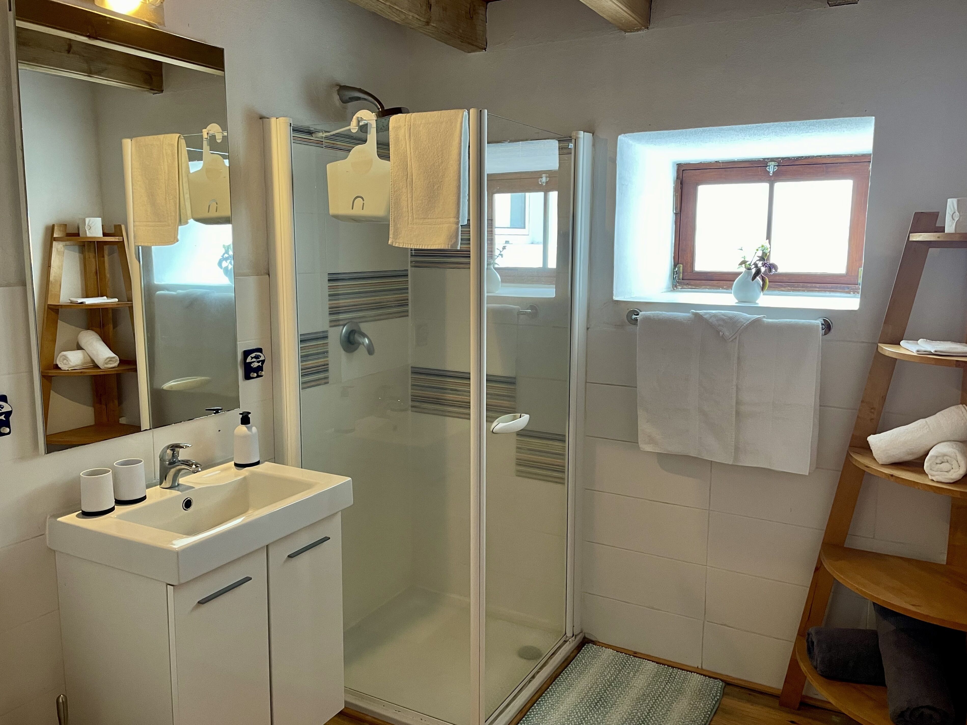A modern bathroom with a glass shower enclosure, a sink with a mirror, and a wooden shelf with towels.