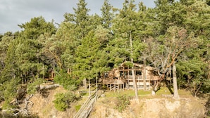 A cabin with a wooden deck and a bridge over a river, surrounded by dense forest. - San Juan Island, Neil Bay #800 (Friday Harbor)