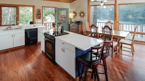 A spacious kitchen with wooden flooring, a large island, and a dining area with wooden chairs and a table. - San Juan Island, Neil Bay #800 (Friday Harbor)