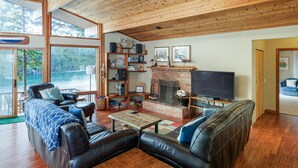 A spacious living room with a fireplace, leather sofas, wooden flooring, and large windows overlooking a lake. - San Juan Island, Neil Bay #800 (Friday Harbor)
