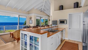A modern kitchen with a large island, white cabinetry, and a view of the ocean.