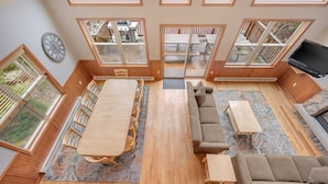 A spacious living area with a large wooden dining table, multiple sofas, and a TV. - Acorn by PMR, 6 BR Mountain Lodge, Lake View, Hot Tub, Game Room, Fire Pit (Lake Harmony)