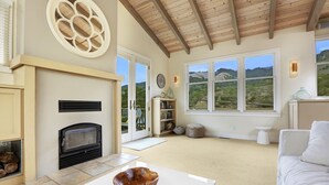 A living room with a fireplace, large windows, and a view of the outdoors. - Immaculate Beach House with Great Views Of Mt Tam (Stinson Beach)