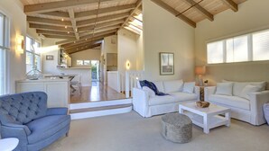 A spacious living area with a high ceiling, white furniture, and a view into the kitchen. - Immaculate Beach House with Great Views Of Mt Tam (Stinson Beach)