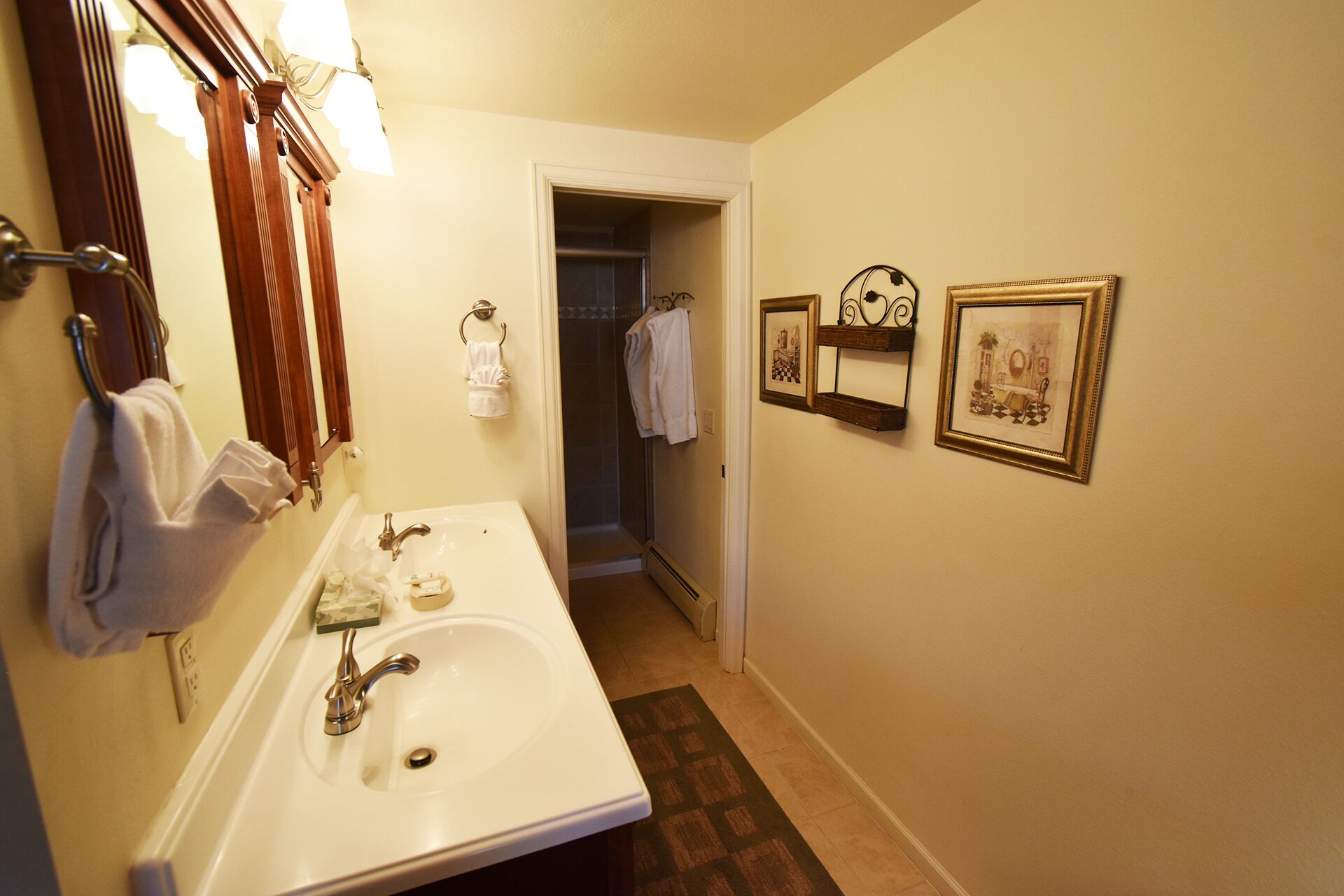 Une salle de bain équipée d’un lavabo, d’un miroir, d’un porte-serviettes et de tableaux encadrés accrochés au mur.