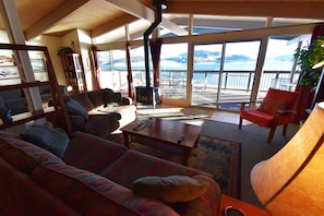 A cozy living room with a sofa, armchairs, and a fireplace. Large windows offer a view of the outdoors. - On Lake! Top Floor Views, Deck! Elevator, Hot Tub. Walk to Concerts, Marina (Dillon)