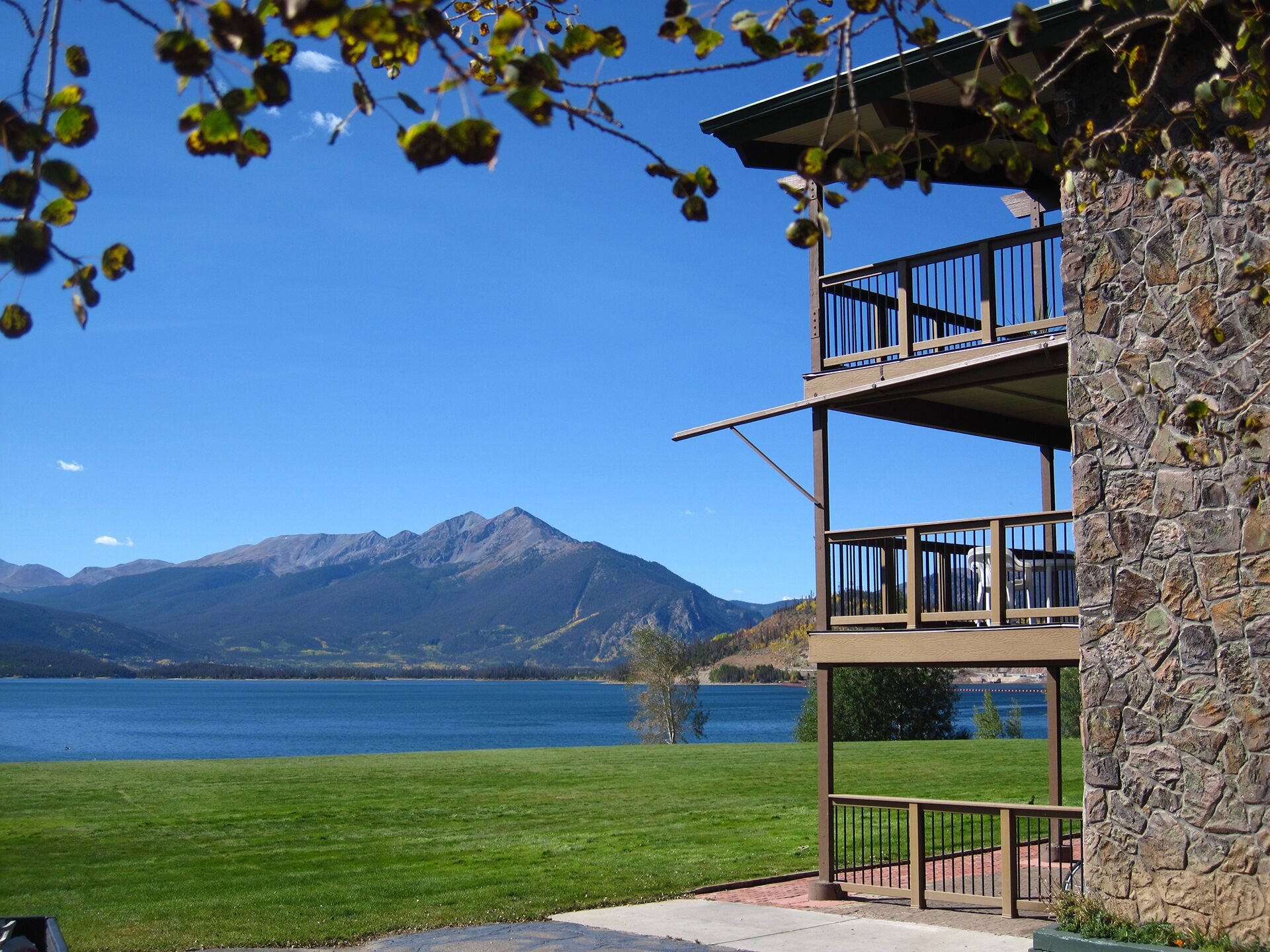 Un immeuble à plusieurs étages, doté d’une façade en pierre et de balcons donnant sur un lac et des montagnes.