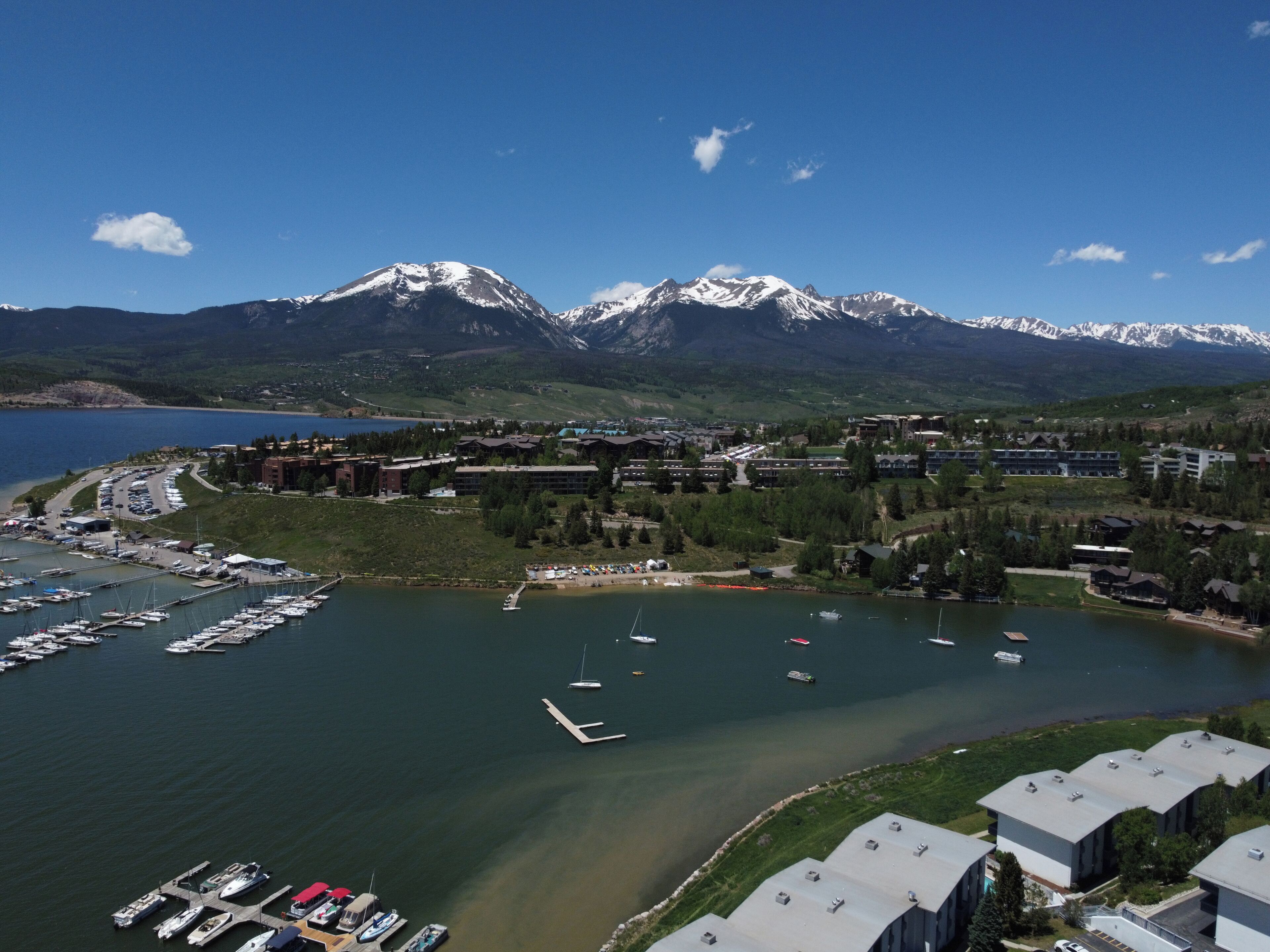 A marina with boats, a mountain range in the background, and buildings with flat roofs.