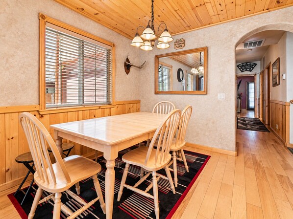 A dining area with a wooden table and chairs, a window with blinds, a wall-mounted mirror, and a 'No Smoking' sign.