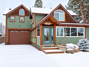 A two-story cabin with a green exterior, a brown garage, and a sign reading 'Casa Bella.'