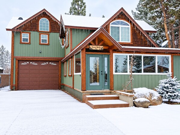 A two-story cabin with a green exterior, a brown garage, and a sign reading 'Casa Bella.'