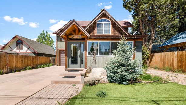 Une maison en bois à deux étages, dotée d’un porche à l’avant, d’un petit arbre et d’une allée pavée.