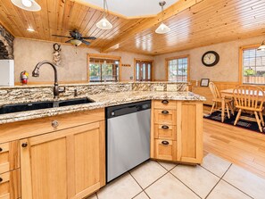 A kitchen with wooden cabinets, a granite countertop, a dishwasher, and a dining area with a table and chairs.