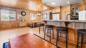 Une cuisine avec des meubles en bois, un coin repas avec une table et des chaises, et un bar avec des tabourets.