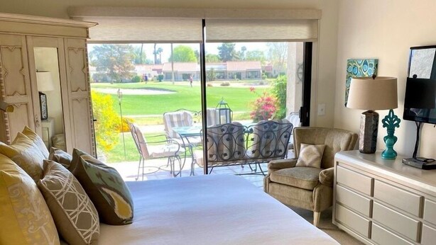A bedroom with a large bed, a dresser, a TV, and a balcony with outdoor furniture. - Palm Desert Resort & Country Club I (Palm Desert)