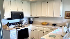 A kitchen with white cabinets, a black microwave, a coffee maker, and a sink. - Palm Desert Resort & Country Club I (Palm Desert)